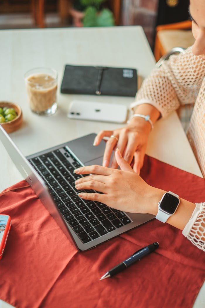 Close-up of a woman working on a laptop with a smartwatch, emphasizing modern technology and productivity at a cozy desk.